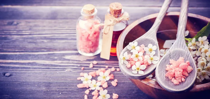 Flacons d’huiles essentielles, fleurs blanches et sels roses sur une table en bois